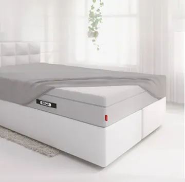 Die BODYGUARD® Boxspring Matratze ist bis auf eine Ecke mit dem Spannbettlaken extra hoch bezogen und liegt auf einem Boxspringbett in einem hellen Schlafzimmer.