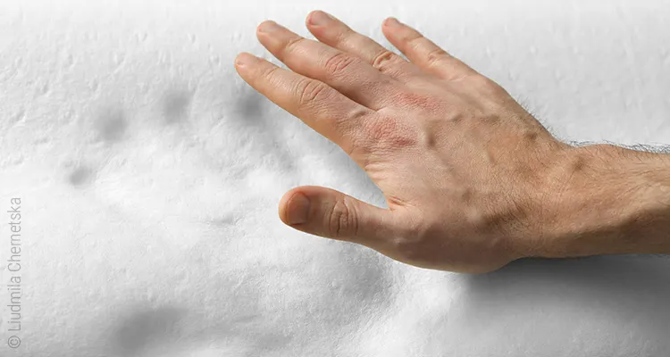Eine Hand schwebt über einer Schaumstoffmatratze aus Viscoschaum in der der Handabdruck noch sichtbar ist