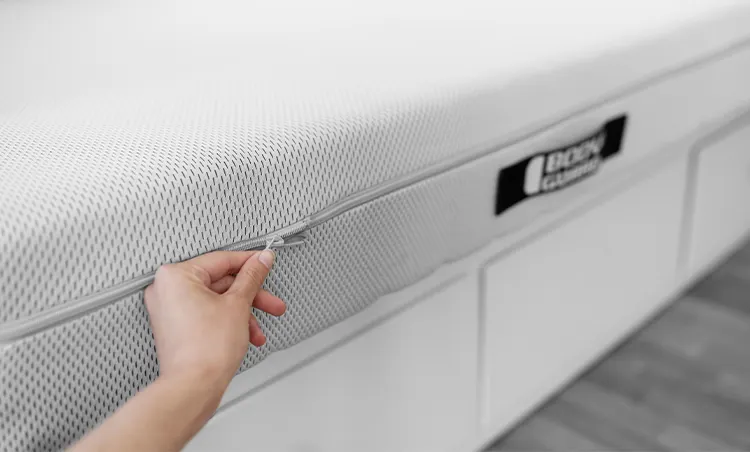 Eine Hand greift mit zwei Fingern nach dem den Reißverschluss einer BODYGUARD Matratze.