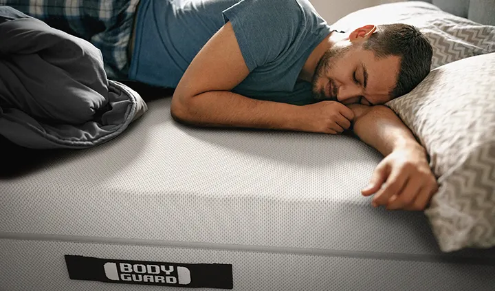 Eine Person liegt bäuchlings auf einer BODYGUARD Matratze und hat dabei einen Arm ausgestreckt, den anderen angewinkelt.