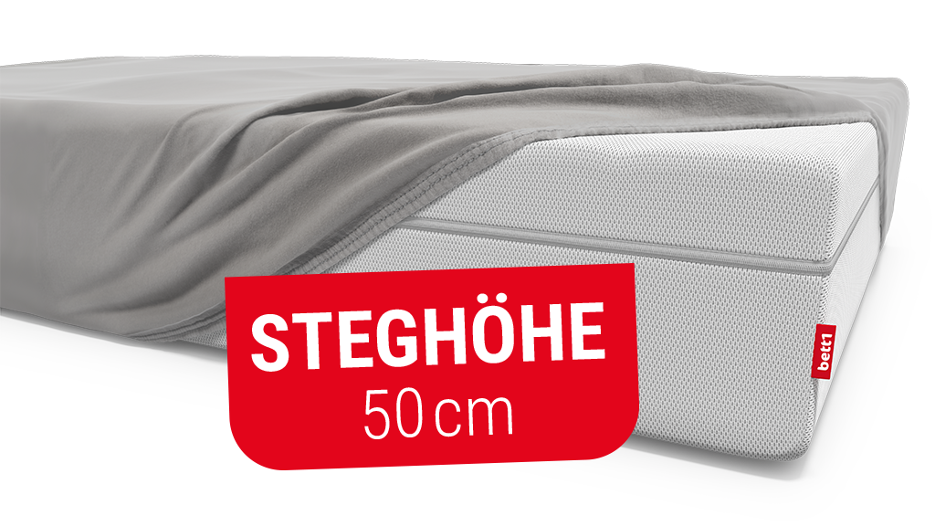Eine hohe Matratze ist bis auf eine Ecke mit einem Spannbettlaken bezogen. Text: Steghöhe 50 cm