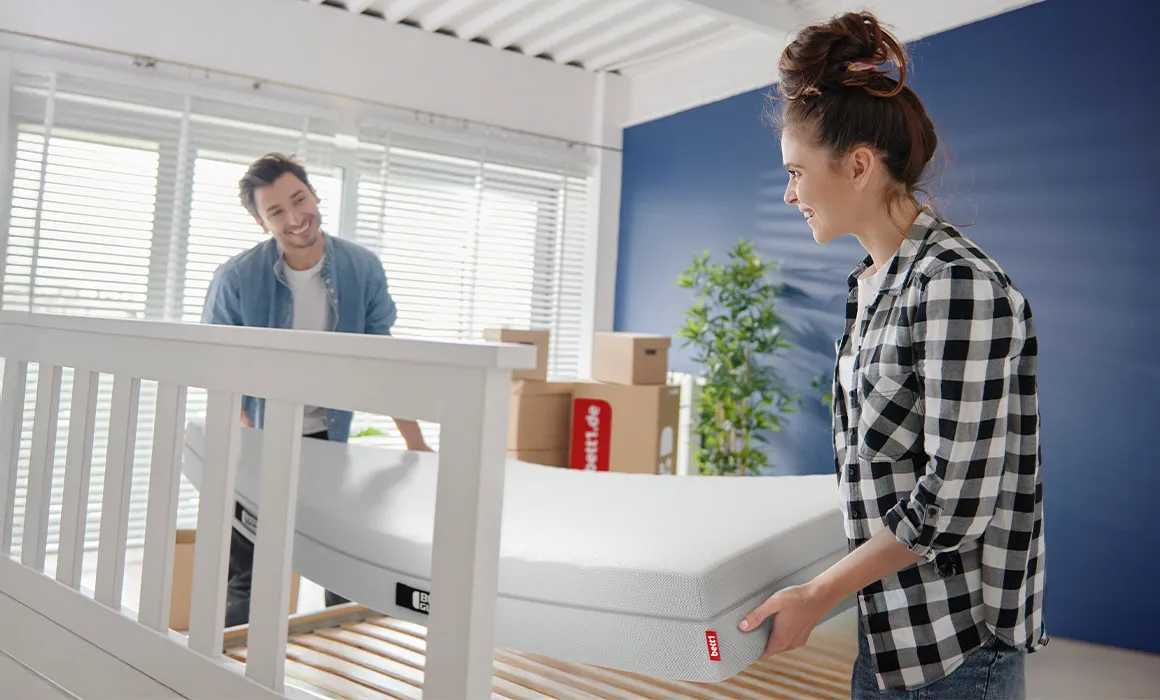 Zwei Personen heben eine Matratze auf einen Lattenrost