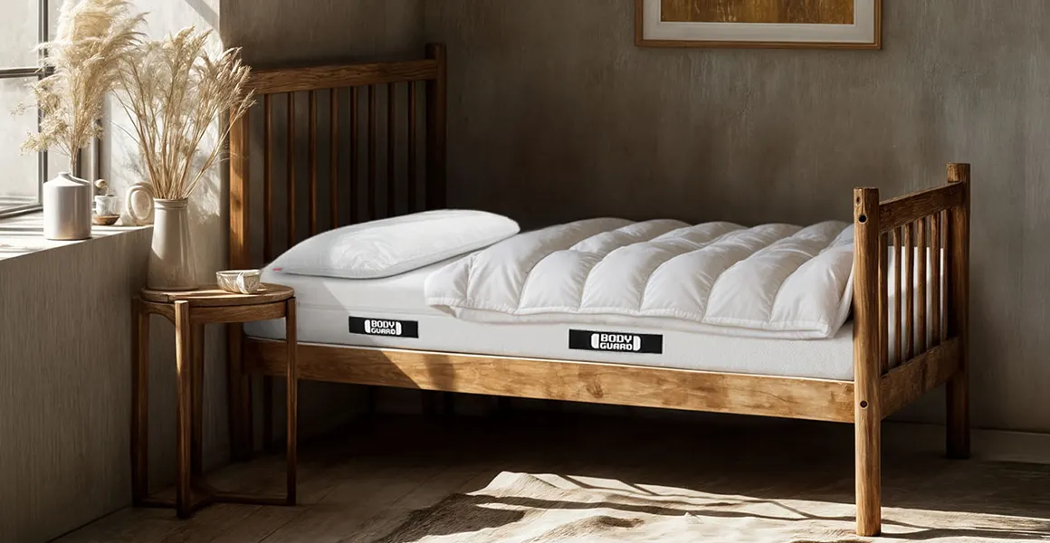 Ein rustikal anmutendes Zimmer mit einem kurzen Holzbett. Darauf liegt die BODYGUARD Anti-Kartell-Matratze mit Decke und Kissen.