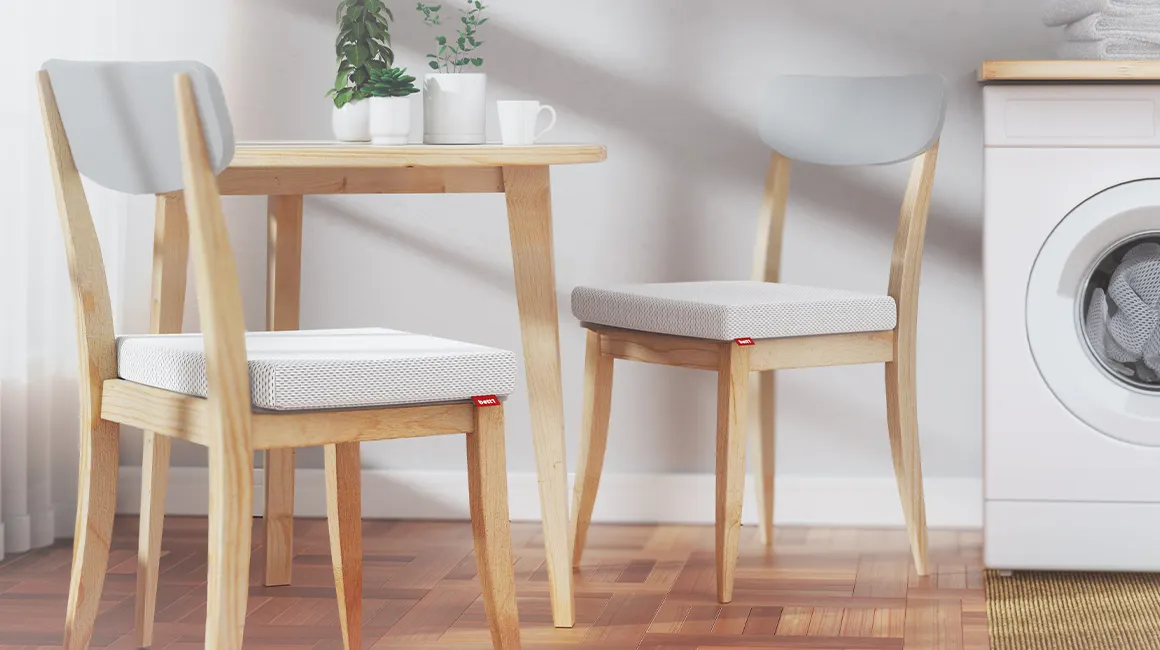 An einem Küchentisch stehen zwei Küchenstühle, auf denen das BODYGUARD Sitzkissen 40x40 liegt.