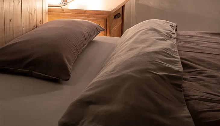 Foto: In einem warm beleuchteten Schlafzimmer liegen Kopfkissen und Decke bezogen mit Winterbettwäsche aus Flanell im Bett. Die Bettdecke ist ein wenig zurückgeklappt, sodass die dunkle und helle Seite der Flanellbettwäsche sichtbar sind.