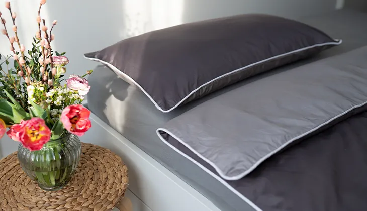 Foto: Ein Bett, bezogen mit der Sommerbettwäsche aus Satin. Die Bettdecke ist ein wenig zurückgeklappt, sodass die dunkle und helle Seite der Satinbettwäsche sichtbar sind.