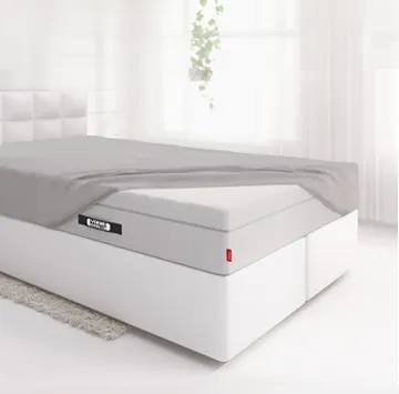 Die BODYGUARD® Boxspring Matratze ist bis auf eine Ecke mit dem Spannbettlaken extra hoch bezogen und liegt auf einem Boxspringbett in einem hellen Schlafzimmer.