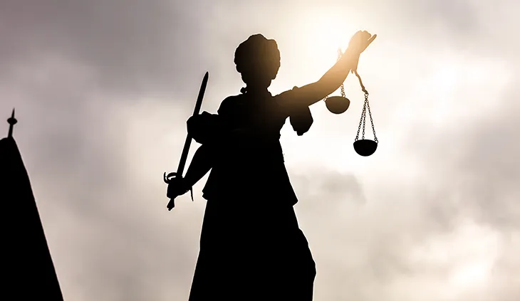 Eine Statue der römischen Göttin Justitia wird von hinten von der Sonne angestrahlt.