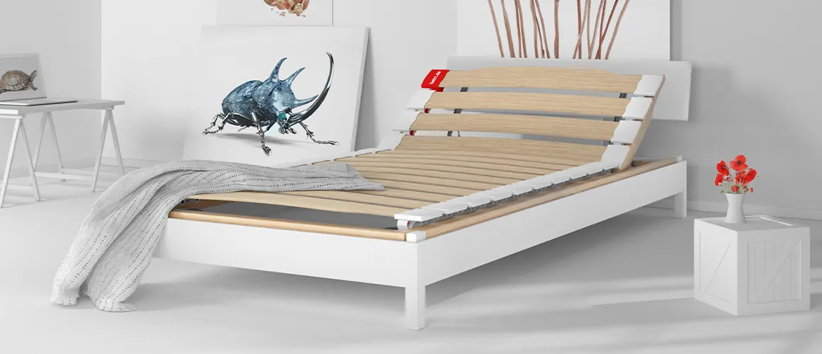 Ein Schlafzimmer mit zahlreichen bemalten Leinwänden. In der Mitte der BODYGUARD Lattenrost mit hochgestelltem Kopfteil in einem Bett ohne Matratze.