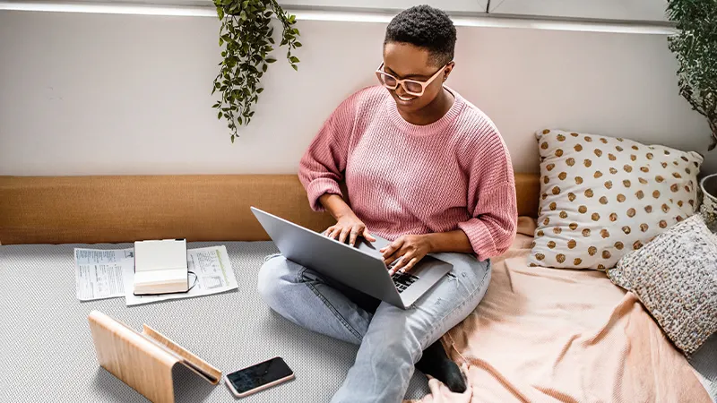 Foto: Eine Person sitzt mit einem aufgeklappten Laptop auf den Beinen auf dem Boden. 