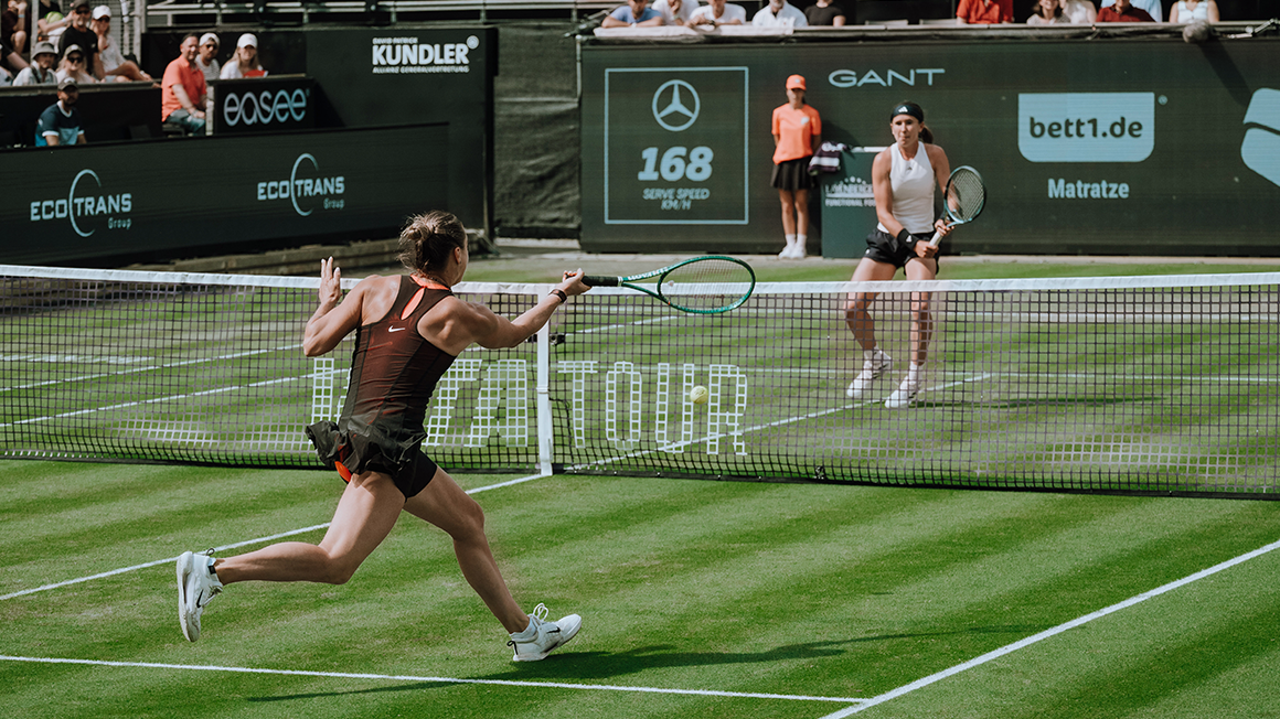 Auf einem Rasentennisplatz spielen zwei Frauen Tennis.