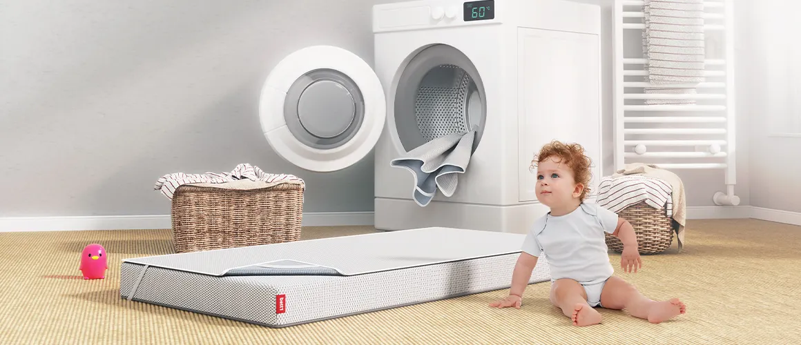 Der Nässeschutz auf der Kindermatratze vor der ein Baby sitzt.