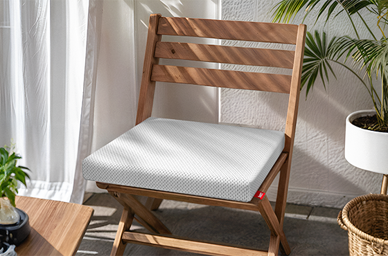 Ein hölzerner Klappstuhl steht in der Sonne. Auf der Sitzfläche liegt das BODYGUARD®Sitzkissen. Daneben stehen Pflanzen. 