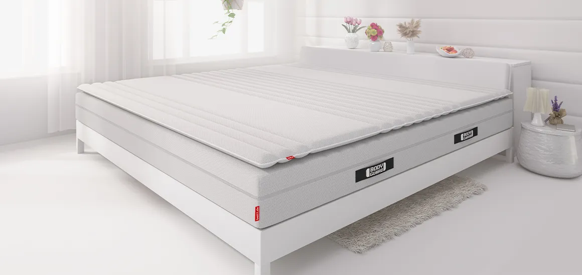 In einem Bett liegt die BODYGUARD® Matratze und darauf der BODYGUARD® Topper.