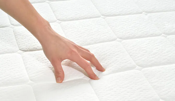 Eine Person drückt mit den Fingerspitzen auf die Oberfläche einer Matratze.
