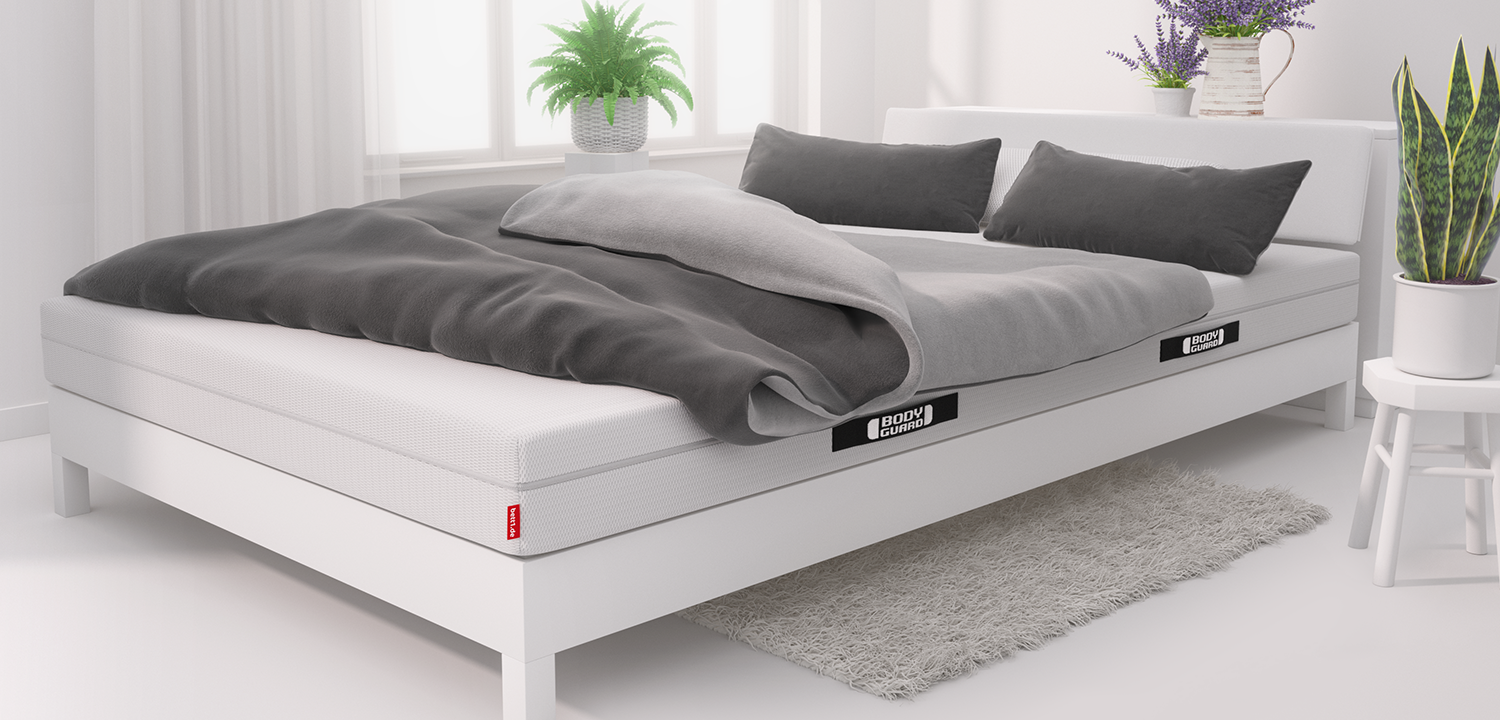 In einem hellen Schlafzimmer steht ein Doppelbett mit der Matratze 140x220 cm, einer Paardecke und zwei Kissen darauf.