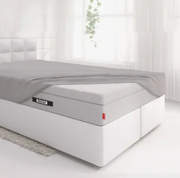 Die BODYGUARD® Boxspring Matratze ist bis auf eine Ecke mit dem Spannbettlaken extra hoch bezogen und liegt auf einem Boxspringbett in einem hellen Schlafzimmer.