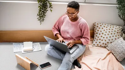 Foto: Eine Person sitzt mit einem aufgeklappten Laptop auf den Beinen auf dem Boden. 