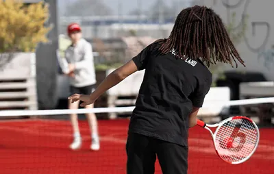 Foto: Ein Kind spielt einen Tennisball über ein Netz zu einem anderen Kind.