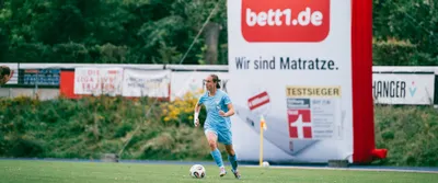 Foto: Spielerinnen mit unterschiedlichen Trikots auf einem Rasen.