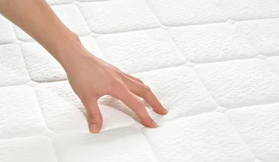 Eine Person drückt mit den Fingerspitzen auf die Oberfläche einer Matratze.